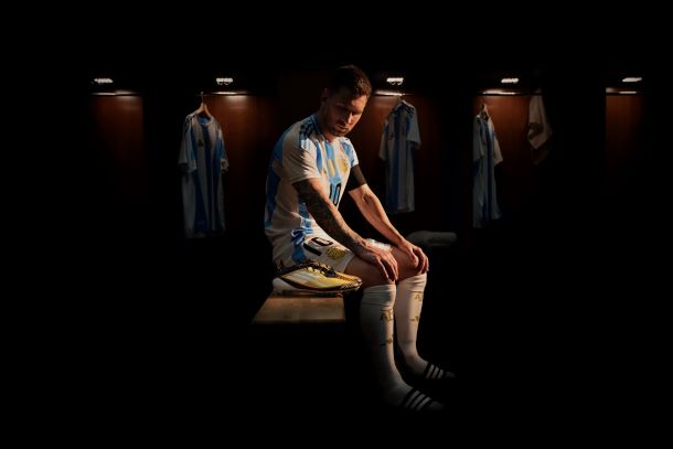 Messi wearing his Argentina Kit, while sitting next to the adidas F50 Triunfo Dorado Football Boots in Gold.